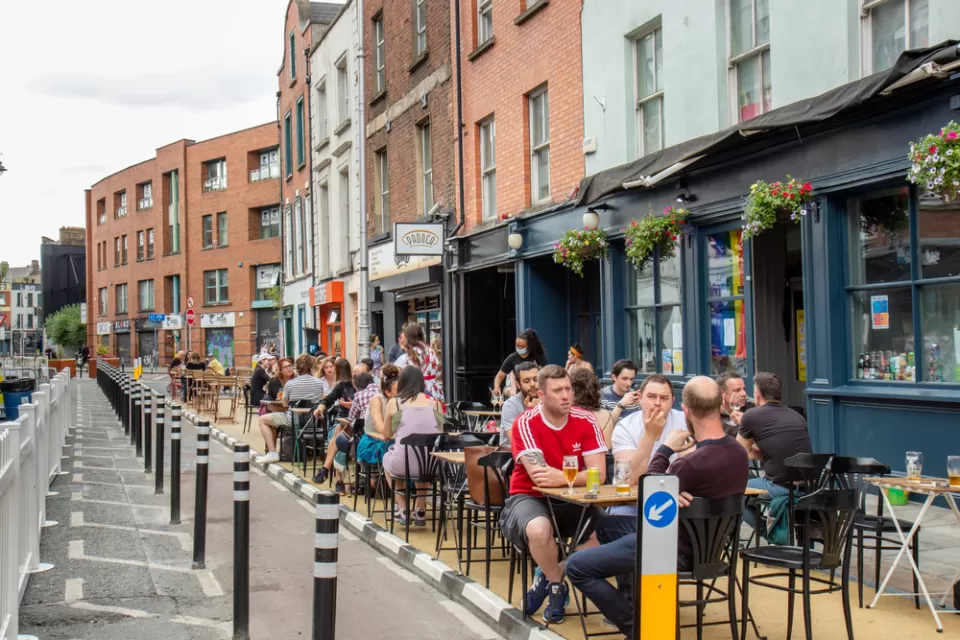 People sitting at outdoor dining tables next to bike lane protected by delineators and three-story buildings in Dublin, Ireland